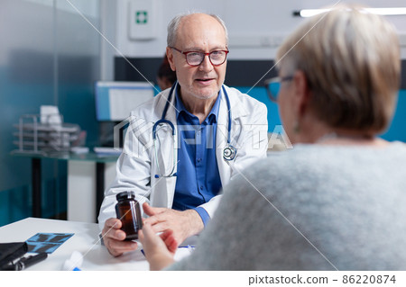 Medic giving bottle of pills to senior patient at checkup appointment in cabinet 86220874