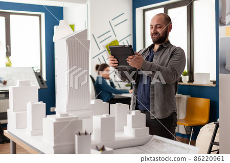 Bearded professional architect looking at tablet in front of white foam building model 86220961