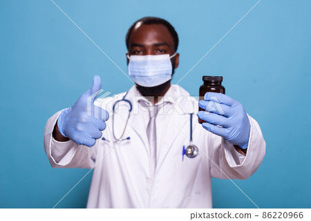 Focus on doctor holding pill bottle giving thumbs up wearing face mask 86220966