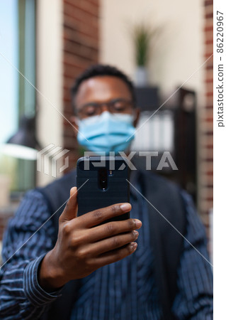 Closeup of entrepreneur holding smartphone in video call conference wearing covid protective mask Closeup of entrepreneur holding smartphone in video call conference wearing covid protective mask 86220967
