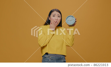 Asian woman with anxiety checking time on clock in studio Asian woman with anxiety checking time on clock in studio 86221013