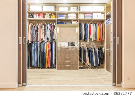 Modern wooden wardrobe with clothes hanging on rail in walk in closet 86221777