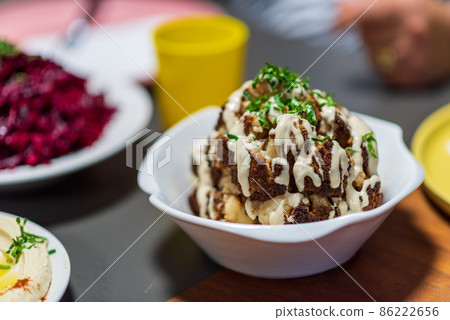 One whole head of roasted cauliflower with roasting ingredients and tahini sauce. Middle Eastern Health Diet. Mediterranean and Balkan food. One whole head of roasted cauliflower with roasting ingredients and tahini sauce. Middle Eastern Health Diet. Mediterranean and Balkan food. 86222656