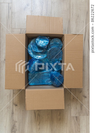 Glassware wrapped with blue wrapping nylon at the bottom of a cardboard box. Glassware wrapped in a box Glassware wrapped with blue wrapping nylon at the bottom of a cardboard box. Glassware wrapped in a box 86222672