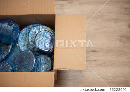 Glassware wrapped with blue wrapping nylon at the bottom of a cardboard box. Glassware wrapped in a box Glassware wrapped with blue wrapping nylon at the bottom of a cardboard box. Glassware wrapped in a box 86222691