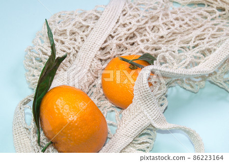 Ripe tangerines in a string bag on a blue background. Fruits in eco-friendly packaging Ripe tangerines in a string bag on a blue background. Fruits in eco-friendly packaging 86223164