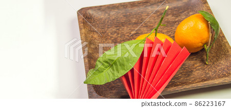 Chinese New Year, composition with tangerines, funny origami made of red paper on a dark wooden plate on a white background, space for text on the left Chinese New Year, composition with tangerines, funny origami made of red paper on a dark wooden plate on a white background, space for text on the left 86223167