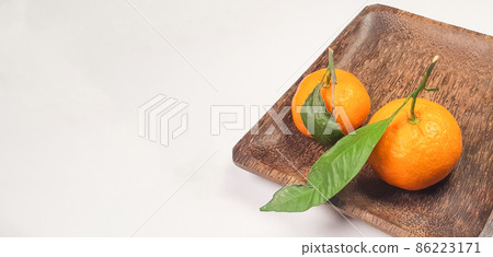 Two fresh ripe tangerines with leaves and branches on a dark square wooden plate, close-up, space for text on the left Two fresh ripe tangerines with leaves and branches on a dark square wooden plate, close-up, space for text on the left 86223171