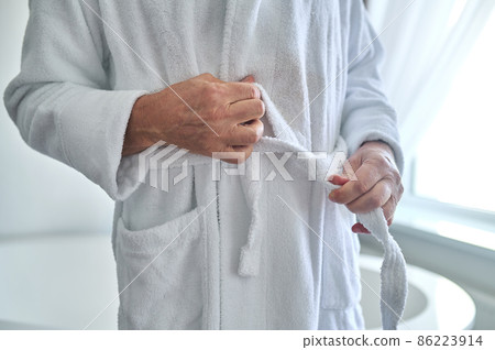 Caucasian man belting the white terry bathrobe 86223914