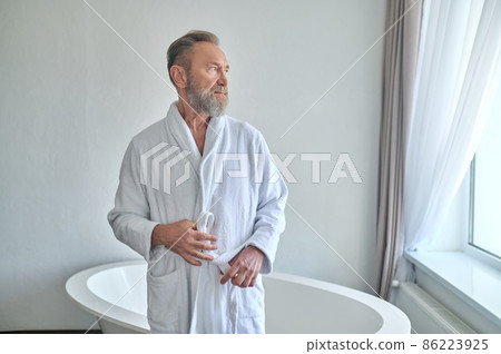Tranquil pensive adult male belting his towelling robe in the bathroom 86223925