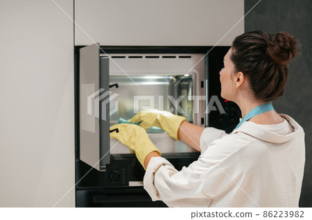 A woman in yellow gloves cleaning the oven 86223982