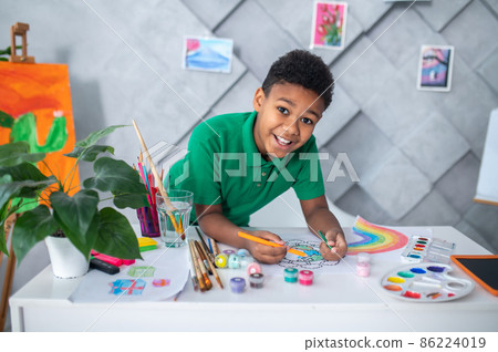 Boy standing at table drawing and looking at camera Boy standing at table drawing and looking at camera 86224019