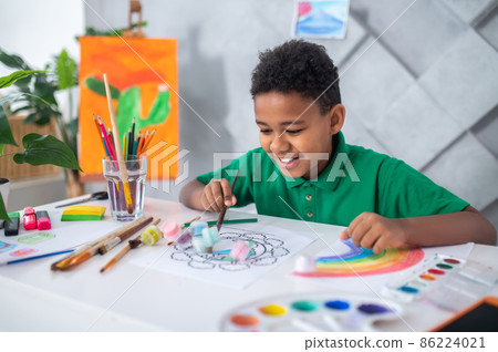 Boy sitting at table pushing tubes of paint Boy sitting at table pushing tubes of paint 86224021