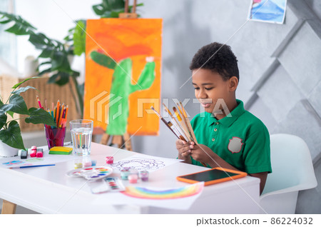 Boy looking at brushes sitting at table Boy looking at brushes sitting at table 86224032