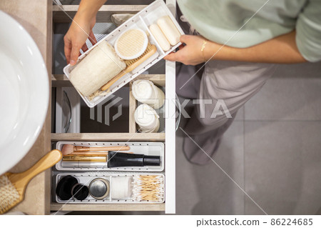 Top view of woman hands neatly organizing bathroom amenities and toiletries in drawer in bathroom. Top view of woman hands neatly organizing bathroom amenities and toiletries in drawer in bathroom. 86224685