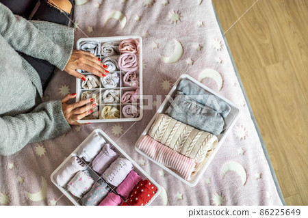 Top view mother hands neatly putting female kid clothes into plastic case box comfortable storage Top view mother hands neatly putting female kid clothes into plastic case box comfortable storage 86225649