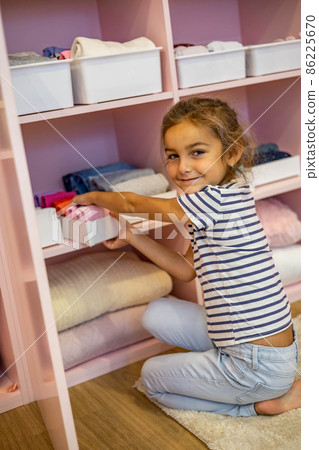 Top view little girl neatly folded clothes into case box for comfortable vertical storage on shelves Top view little girl neatly folded clothes into case box for comfortable vertical storage on shelves 86225670