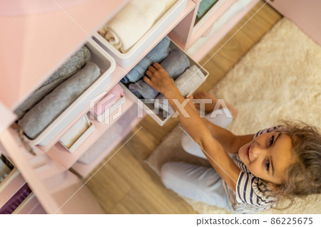 Top view little girl neatly folded clothes into case box for comfortable vertical storage on shelves Top view little girl neatly folded clothes into case box for comfortable vertical storage on shelves 86225675