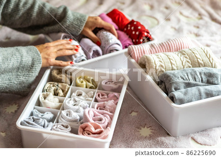 Top view mother hands neatly putting female kid clothes into plastic case box comfortable storage Top view mother hands neatly putting female kid clothes into plastic case box comfortable storage 86225690