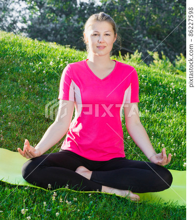 Fitness woman in pink T-shirt is sitting and meditating Fitness woman in pink T-shirt is sitting and meditating 86227598