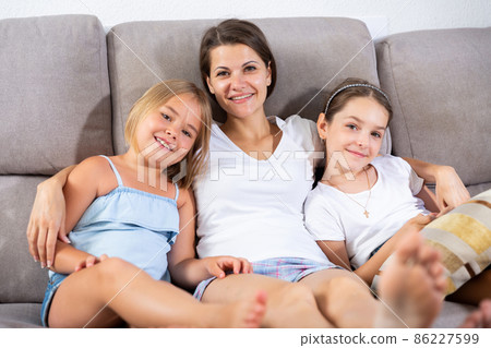 Woman and two daughters resting on sofa 86227599