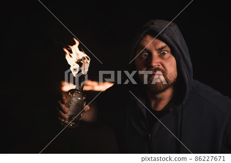 The man in the hood is holding a burning bottle. Molotov cocktail. The man in the hood is holding a burning bottle. Molotov cocktail. 86227671