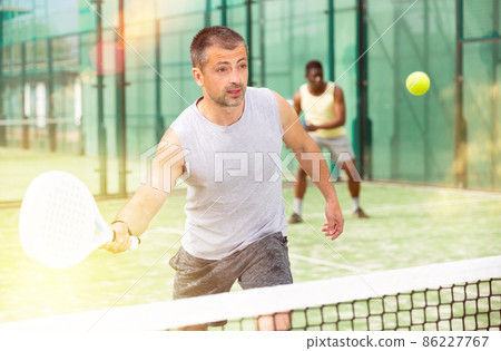 Athletic mens plays padel. View through tennis net Athletic mens plays padel. View through tennis net 86227767