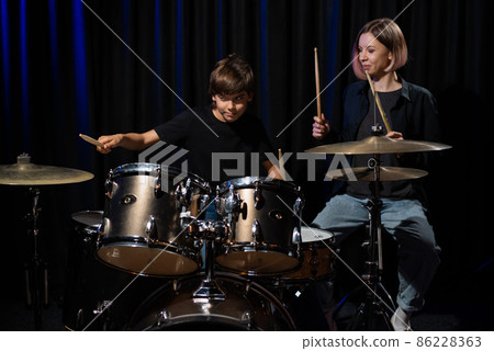 Young caucasian woman teaches a boy to play the drums in the studio on a black background. Music school student 86228363
