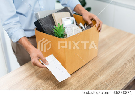 Resignation Concept The male officer standing, putting his box of his belongs on the desk and handing the white letter to someone Resignation Concept The male officer standing, putting his box of his belongs on the desk and handing the white letter to someone 86228874