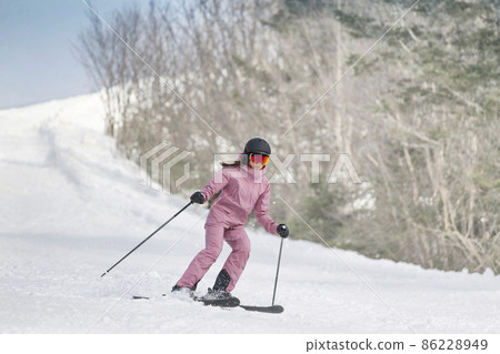 Skiing - Woman on ski. Alpine ski concept - skier skiing downhill at mountain snow covered ski trail slopes in winter on perfect powder snow enjoying nature landscape. Elegant pink ski clothing Skiing - Woman on ski. Alpine ski concept - skier skiing downhill at mountain snow covered ski trail slopes in winter on perfect powder snow enjoying nature landscape. Elegant pink ski clothing 86228949