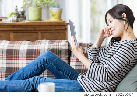 A woman in everyday wear looking at the screen of a tablet device A woman in everyday wear looking at the screen of a tablet device 86230594