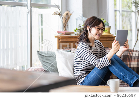 一位穿著日常服裝的女士看著平板電腦的屏幕 86230597