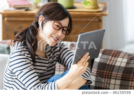 一位穿著日常服裝的女士看著平板電腦的屏幕 86230598