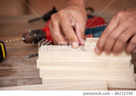 Hands of a carpenter taking measurement of a wooden plank 86232599