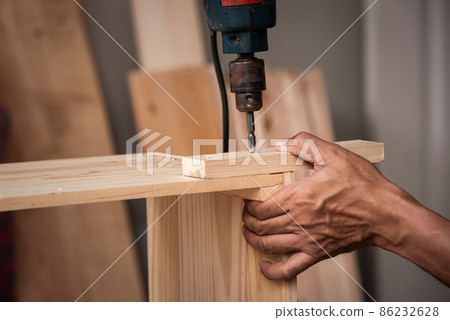 Close-up hands of male artisan drilling lumber in his shop. Concept wood shop of technology and equipment.. Close-up hands of male artisan drilling lumber in his shop. Concept wood shop of technology and equipment.. 86232628