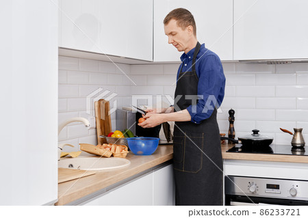 A middle-aged man breaks an egg to make an omelet 86233721
