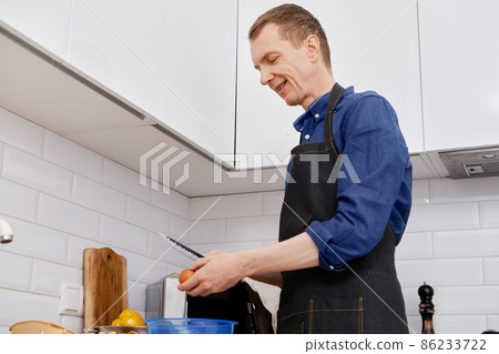 A middle-aged man breaks an egg to make an omelet 86233722