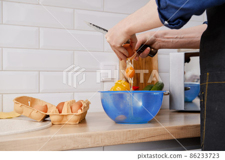A middle-aged man breaks an egg to make an omelet 86233723