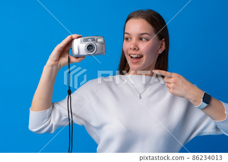 Young caucasian woman holding vintage camera on blue background in studio 86234013