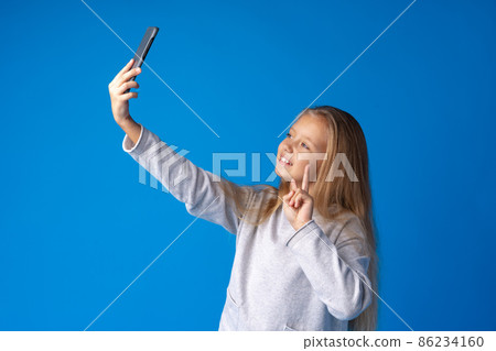 Portrait of an excited little girl taking a selfie isolated over blue background Portrait of an excited little girl taking a selfie isolated over blue background 86234160