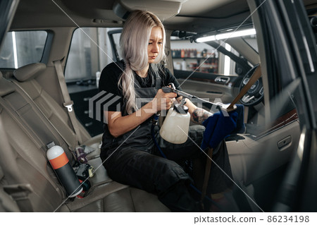 Woman cleaning car salon with polishing spray in car detailing service 86234198
