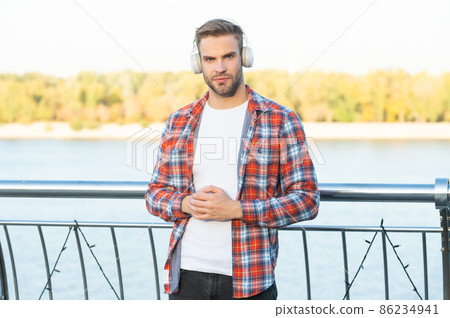 young guy with bristle listen music in headphones outdoor. male fashion model. young guy with bristle listen music in headphones outdoor. male fashion model. 86234941