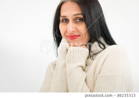 Middle aged woman starting getting grey-haired is posing in studio in sweater on white background, face skin care beauty, middle age skincare cosmetics, cosmetology concept 86235315