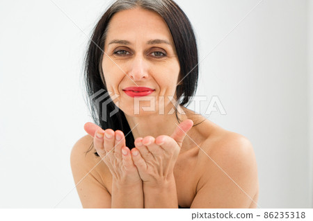Middle aged woman starting getting grey-haired is sending air kiss in studio with naked shoulders on white background, face skin care beauty, middle age skincare cosmetics, cosmetology concept Middle aged woman starting getting grey-haired is sending air kiss in studio with naked shoulders on white background, face skin care beauty, middle age skincare cosmetics, cosmetology concept 86235318