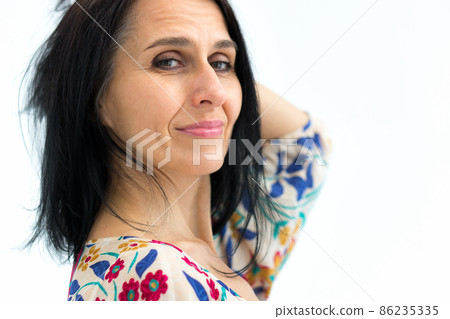Close-up portrait of middle aged woman starting getting grey-haired wearing dress with flowers on white background, middle age sexy lady, cosmetology concept Close-up portrait of middle aged woman starting getting grey-haired wearing dress with flowers on white background, middle age sexy lady, cosmetology concept 86235335