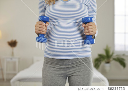 Close up crop of healthy young pregnant woman hold dumbbells do sports. Female train exercise workout during pregnancy time. Physical activity and motherhood concept. Close up crop of healthy young pregnant woman hold dumbbells do sports. Female train exercise workout during pregnancy time. Physical activity and motherhood concept. 86235733