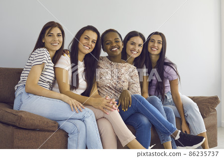 Portrait of smiling multiethnic women sit on couch relax rest on weekend together. Happy millennial gen z diverse multiracial girls friends look at camera show unity friendship. Diversity concept. 86235737