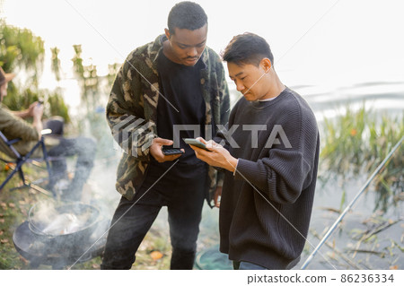 Men using smartphones during resting on pond coast 86236334