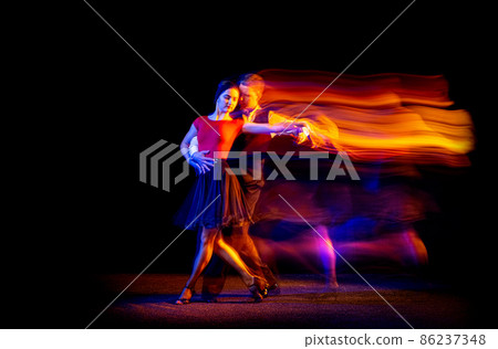 Dynamic portrait of young ballroom dancers dancing Argentine tango isolated on dark background with neon mixed light. Dynamic portrait of young ballroom dancers dancing Argentine tango isolated on dark background with neon mixed light. 86237348