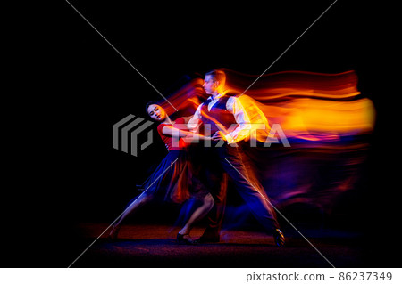 Dynamic portrait of young ballroom dancers dancing Argentine tango isolated on dark background with neon mixed light. 86237349